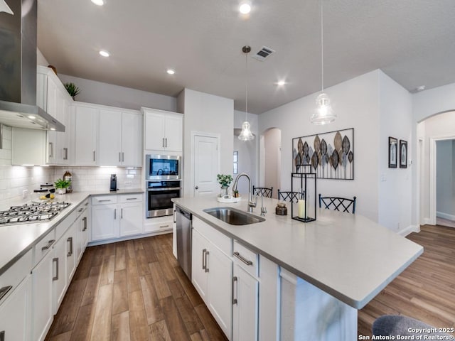 kitchen with arched walkways, appliances with stainless steel finishes, wall chimney range hood, and a sink