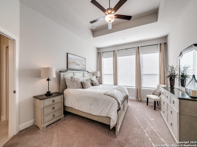 bedroom featuring baseboards, a raised ceiling, light colored carpet, and ceiling fan