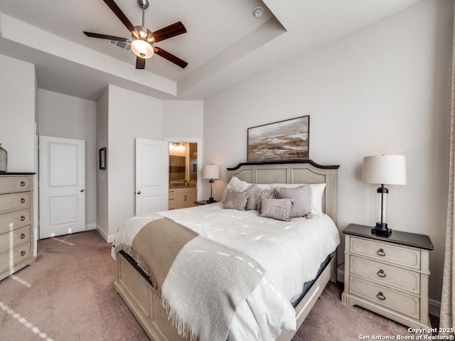 bedroom with baseboards, light colored carpet, a tray ceiling, ensuite bathroom, and a ceiling fan