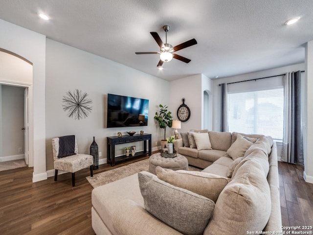 living room featuring baseboards, arched walkways, dark wood-type flooring, and a ceiling fan