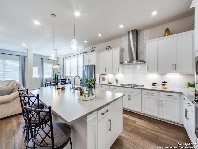 kitchen with decorative backsplash, appliances with stainless steel finishes, a kitchen bar, wall chimney exhaust hood, and open floor plan