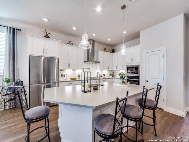 kitchen with a kitchen bar, a sink, dark wood-style floors, stainless steel appliances, and wall chimney exhaust hood