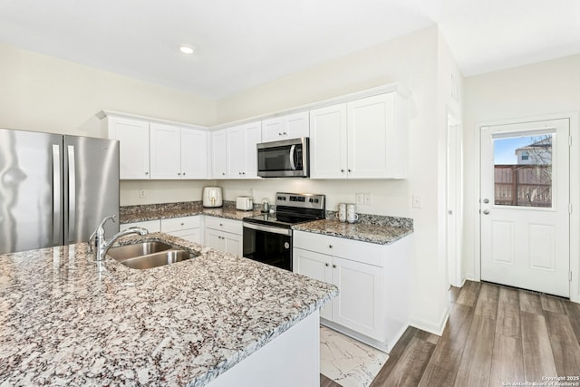 kitchen featuring a sink, light stone counters, appliances with stainless steel finishes, and white cabinetry