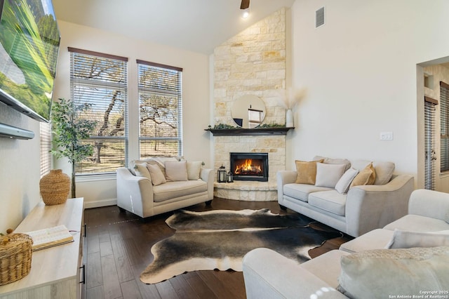 living room featuring a stone fireplace, dark wood-type flooring, visible vents, and high vaulted ceiling