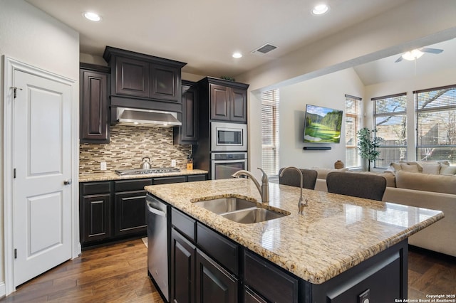 kitchen with wall chimney range hood, dark wood finished floors, open floor plan, stainless steel appliances, and a sink