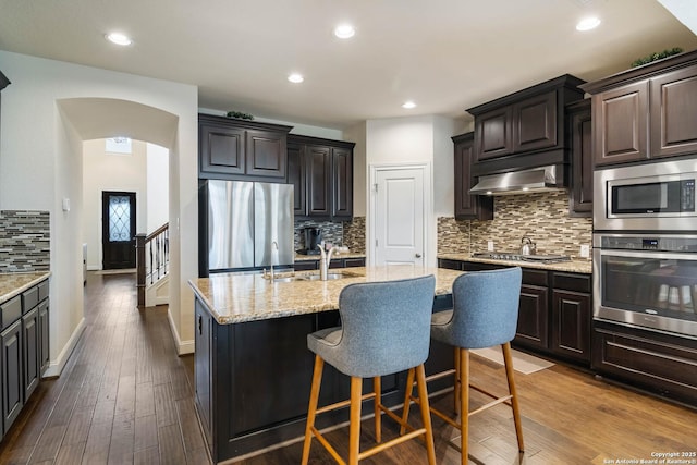 kitchen with an island with sink, a sink, dark wood-style floors, range hood, and stainless steel appliances