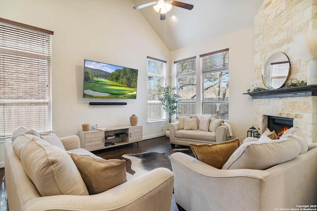 living area with high vaulted ceiling, wood finished floors, a stone fireplace, baseboards, and ceiling fan