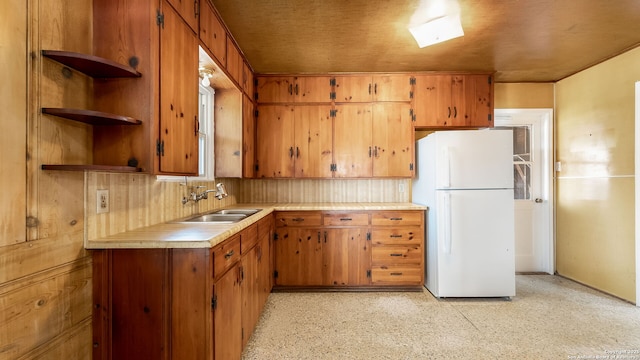 kitchen featuring brown cabinets, a sink, freestanding refrigerator, light countertops, and decorative backsplash