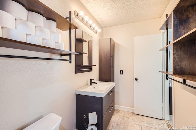 bathroom featuring vanity, toilet, baseboards, and a textured ceiling