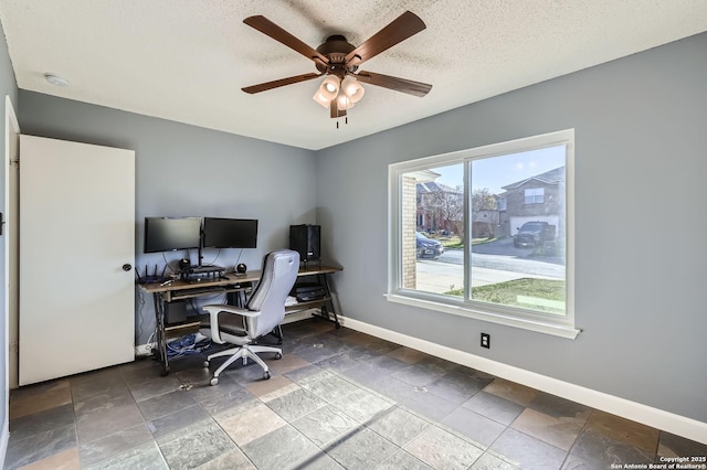 office space featuring stone tile flooring, a textured ceiling, baseboards, and a ceiling fan