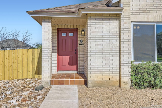 property entrance with fence, brick siding, and roof with shingles