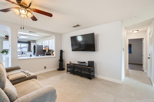 living room featuring visible vents, ceiling fan, a textured ceiling, and baseboards