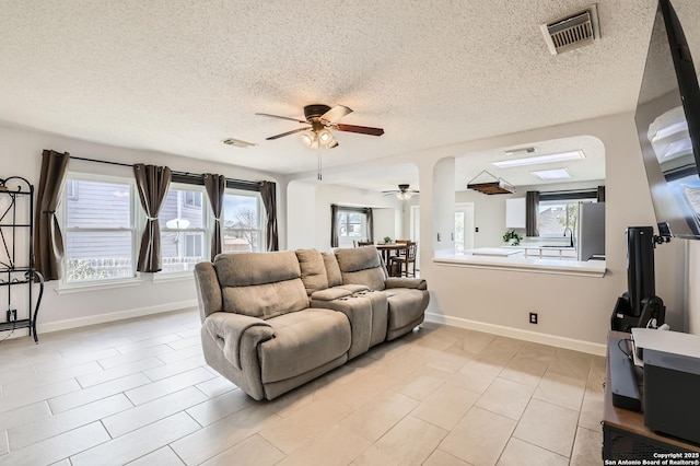 living room featuring visible vents, baseboards, a textured ceiling, and ceiling fan