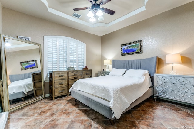 bedroom with tile patterned flooring, visible vents, a ceiling fan, and a tray ceiling