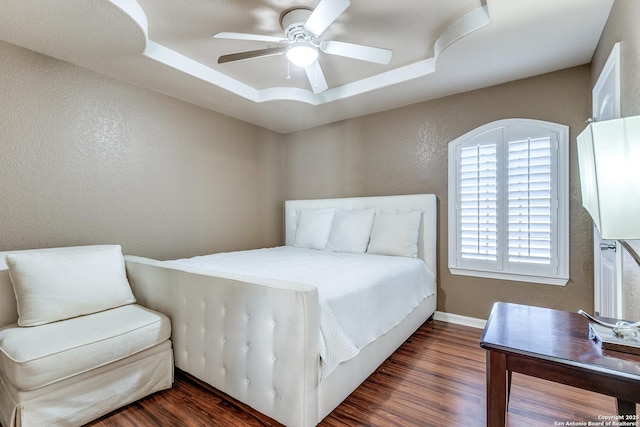 bedroom featuring a textured wall, a ceiling fan, a tray ceiling, and wood finished floors