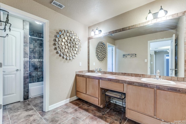 bathroom with double vanity, a textured wall, visible vents, and a sink