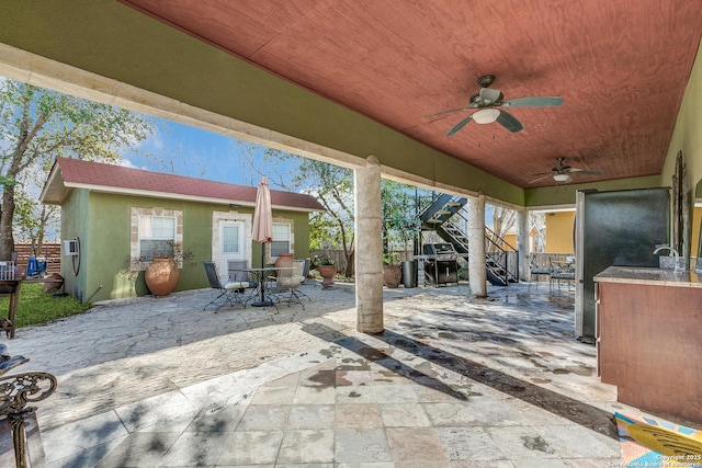 view of patio / terrace with ceiling fan, fence, stairway, outdoor dining area, and an outbuilding