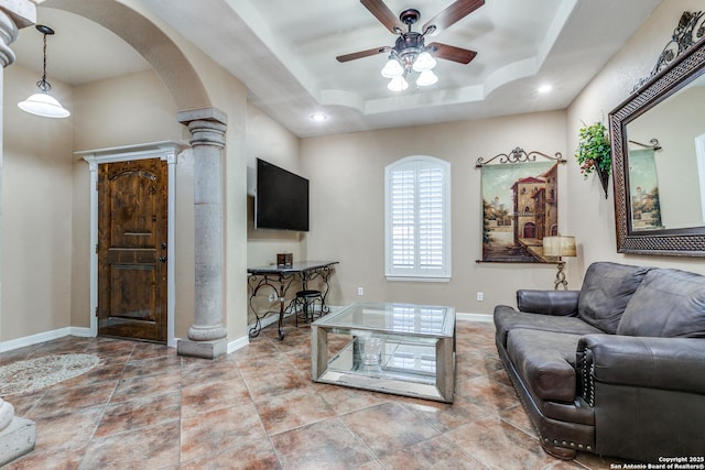 living area with a ceiling fan, baseboards, decorative columns, arched walkways, and a raised ceiling