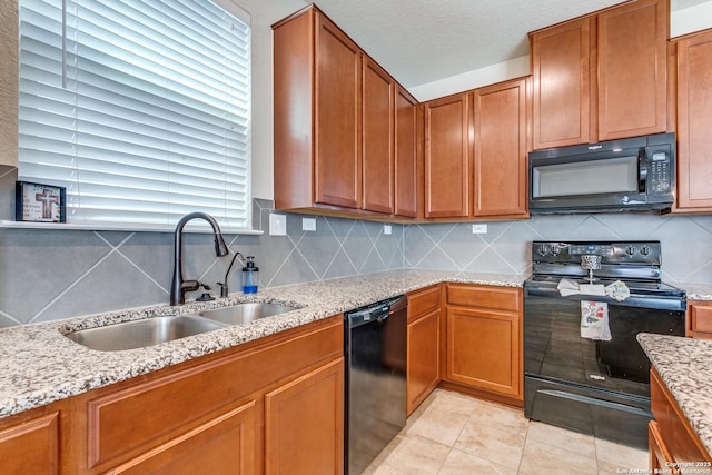 kitchen with light stone counters, brown cabinetry, a sink, black appliances, and tasteful backsplash