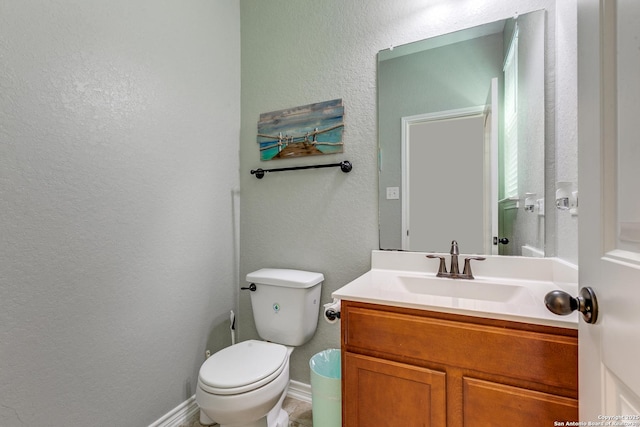 bathroom with toilet, vanity, baseboards, and a textured wall