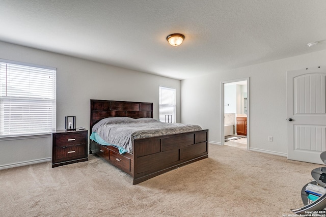 bedroom with a textured ceiling, baseboards, ensuite bathroom, and light carpet