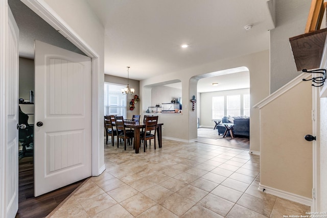 dining space with light tile patterned floors, a chandelier, arched walkways, and baseboards