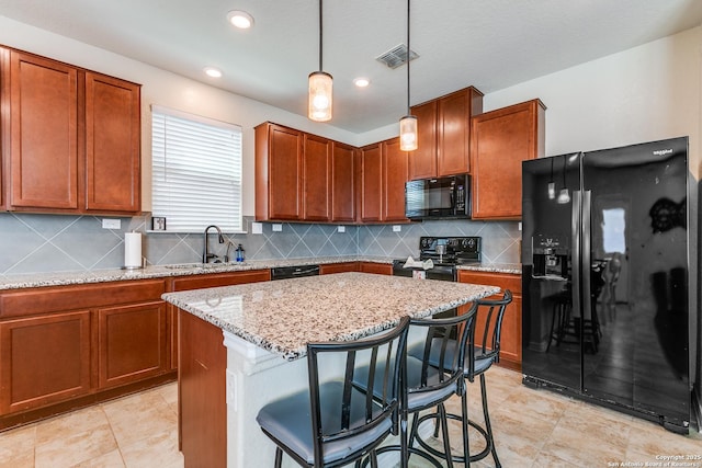 kitchen featuring visible vents, black appliances, light stone counters, a sink, and a kitchen island