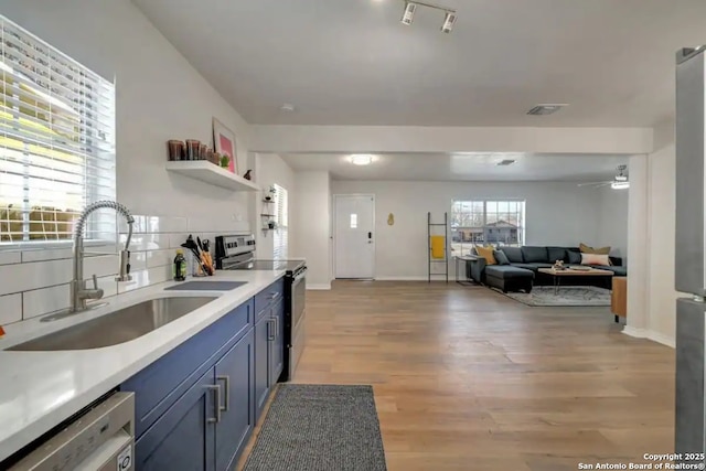 kitchen featuring light wood finished floors, light countertops, decorative backsplash, appliances with stainless steel finishes, and a sink