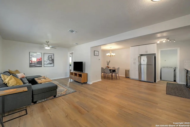 living room featuring washer / clothes dryer, light wood-style floors, visible vents, and baseboards