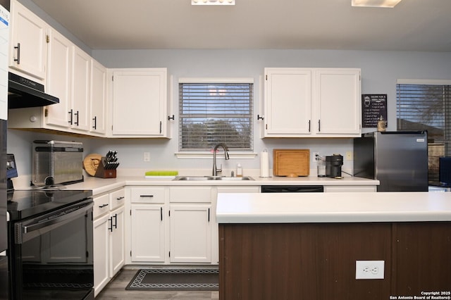 kitchen featuring under cabinet range hood, freestanding refrigerator, electric range, white cabinets, and a sink