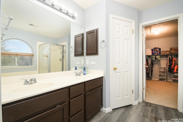 full bathroom with a walk in closet, double vanity, a stall shower, wood finished floors, and a sink