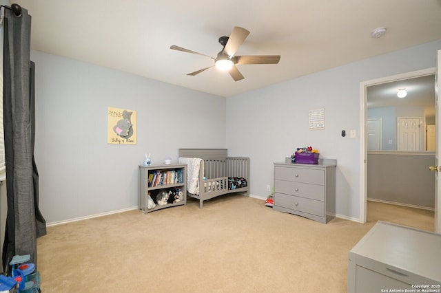 bedroom with baseboards, light carpet, a crib, and a ceiling fan