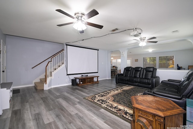 home theater room featuring wood finished floors, arched walkways, visible vents, and ceiling fan