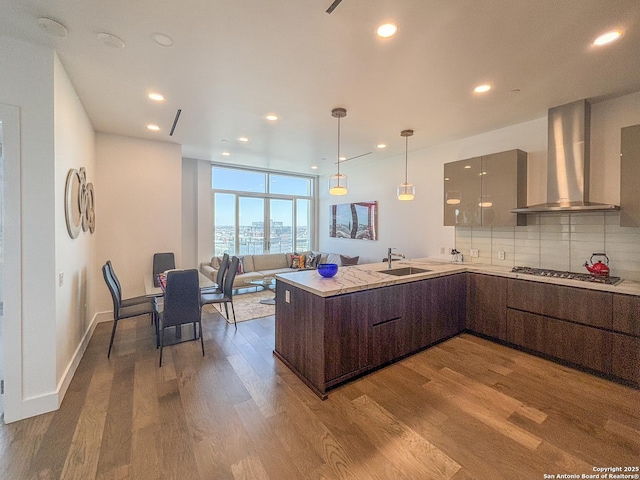 kitchen with wood finished floors, stainless steel gas stovetop, wall chimney exhaust hood, modern cabinets, and backsplash