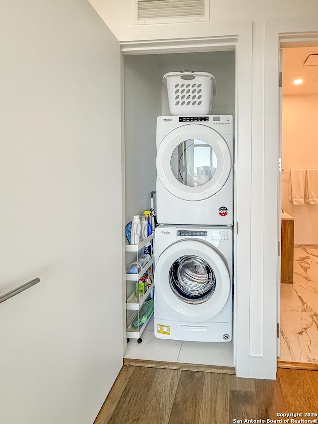 laundry area with visible vents, stacked washer and clothes dryer, wood finished floors, and laundry area