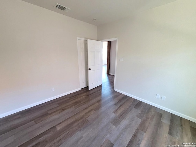 spare room featuring visible vents, dark wood-type flooring, and baseboards