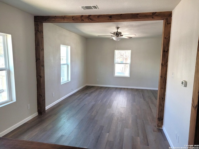 spare room featuring a wealth of natural light, visible vents, baseboards, and dark wood-style floors