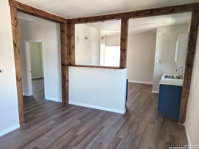 spare room with beam ceiling, dark wood finished floors, baseboards, and a sink