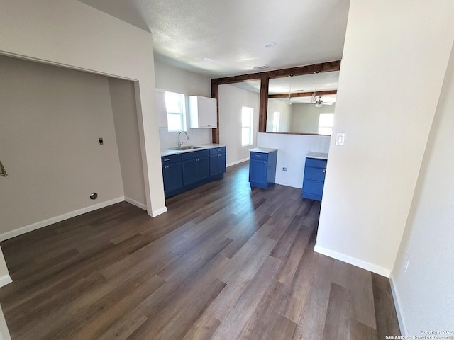 kitchen featuring beam ceiling, dark wood-type flooring, a sink, blue cabinetry, and baseboards