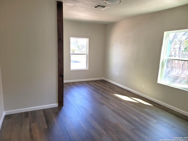 spare room with visible vents, baseboards, dark wood-type flooring, and a textured ceiling