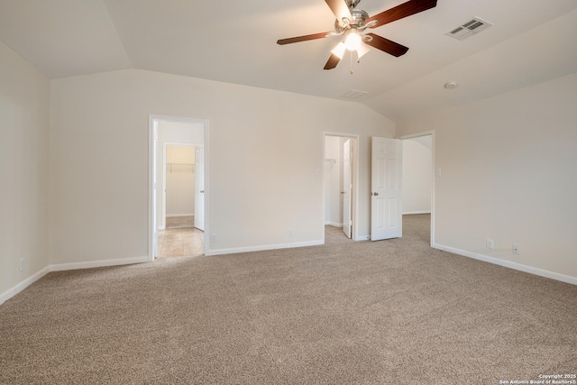 unfurnished bedroom with visible vents, baseboards, vaulted ceiling, a walk in closet, and light colored carpet