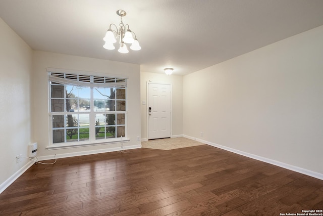 empty room featuring a notable chandelier, baseboards, and wood finished floors