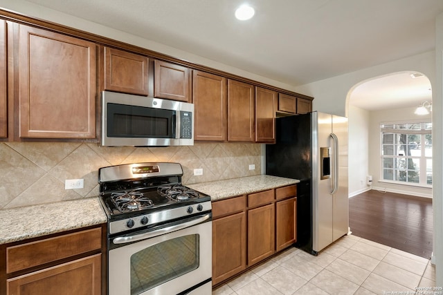 kitchen with light stone counters, backsplash, arched walkways, appliances with stainless steel finishes, and light tile patterned floors