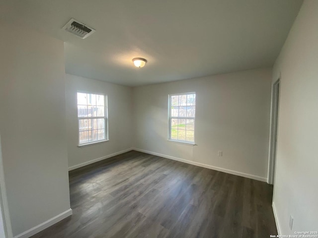 spare room featuring visible vents, baseboards, and dark wood-style flooring