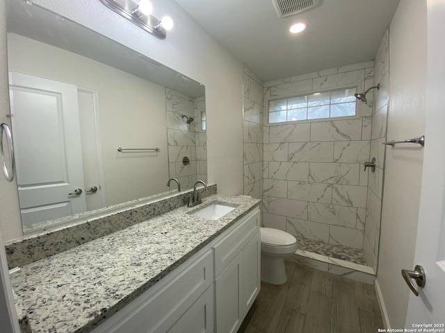 bathroom featuring a tile shower, visible vents, toilet, and vanity