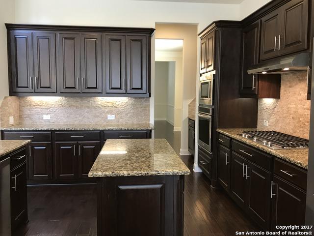 kitchen with dark wood-type flooring, under cabinet range hood, light stone counters, tasteful backsplash, and stainless steel appliances