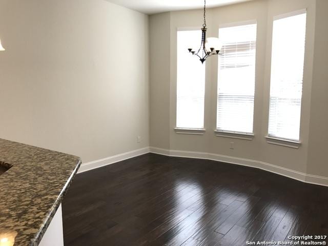 unfurnished dining area featuring dark wood-style floors, baseboards, and a chandelier