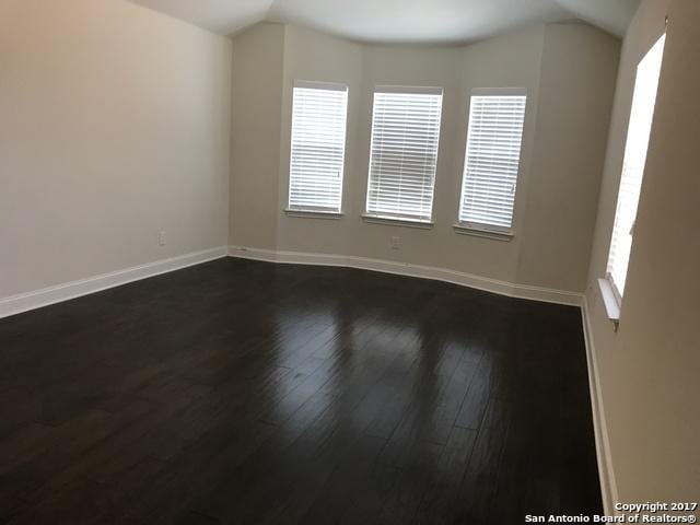 unfurnished room with dark wood finished floors, baseboards, and vaulted ceiling