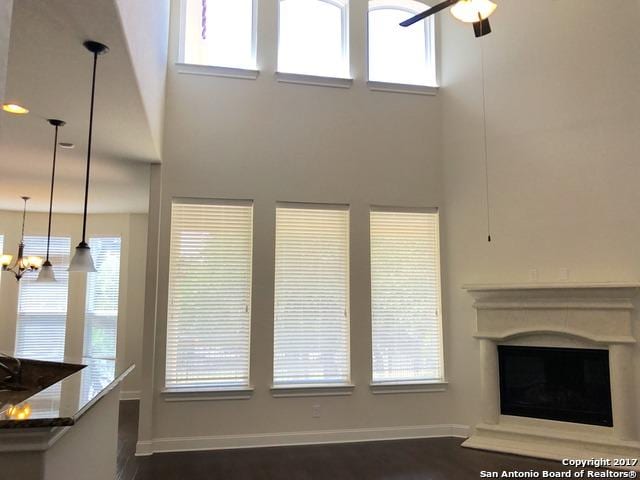 unfurnished living room with ceiling fan with notable chandelier, a healthy amount of sunlight, and baseboards