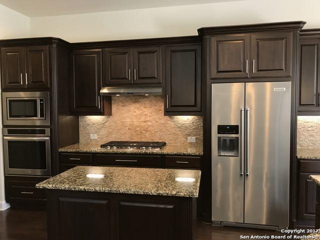 kitchen featuring backsplash, a center island, light stone countertops, under cabinet range hood, and appliances with stainless steel finishes